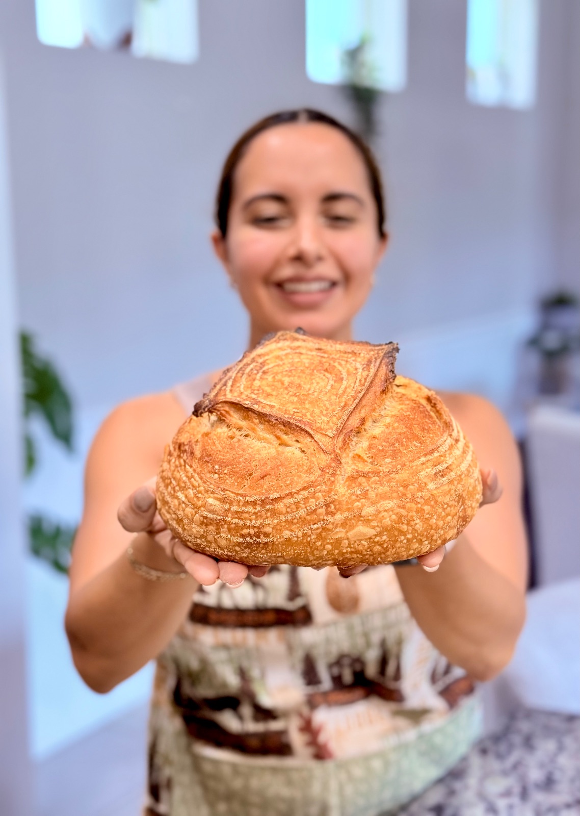 Stephanie Azcona extending a freshly baked sourdough loaf toward the camera